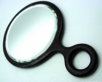 Close-up angled view of the antique hand mirror showing the round beveled glass and ebony wood frame with circular handle.