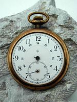 Front of gold filled pocket watch showing white dial with black numbers and missing hands.