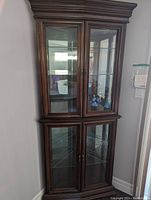 Full view of the tall wood and glass corner display cabinet with closed glass doors.