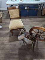 Photo of Eastlake style padded antique chair with diamond patterned upholstery and visible wheels on legs, positioned next to spinning wheel.