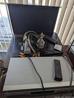 Top-down view of the Panasonic DVD player with remote and multiple AV cables coiled on top, showing device condition and included accessories.