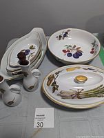 Photo showing an assortment of china pieces including oval serving dishes with fruit patterns and two oil/vinegar cruets with cork stoppers.