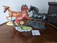 Three porcelain horse figurines displayed on a wooden surface: tan and white The Red Pony, reddish-brown My Friend Flicka, and black Black Beauty.