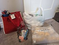 Overall view of the lot including red bag with needles, plastic bag with yarn, felting kits, and pattern booklets on floor.