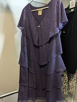 Front view of the purple sparkling layered cocktail dress hung on a rack, showing the tiered design and flutter sleeves.