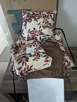 Queen sized bed set spread out showing pillow, sheets, shams, and comforter with brown leaf pattern on cream background.