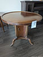 Front view of round solid wood side table with door at base and brass handle.