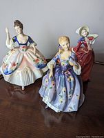 Photo showing the three Royal Doulton porcelain figurines named Nicola, Christine, and Autumn Breezes in detailed period dresses with floral patterns.