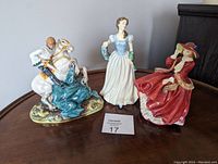 Three figurines displayed on a wooden table with lot card