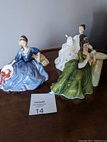 Three Royal Doulton porcelain figurines displayed on a table showing their colors and poses