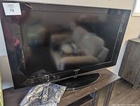 Front view of the 40-inch Samsung television on its stand showing screen, bezel with Samsung logo, and remote control/power cord in plastic bag on side.