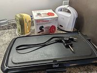 Photo showing Master Chef electric griddle with temperature control dial, Black & Decker hand mixer, and microwave rice cooker box and cooker, arranged on countertop.