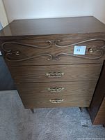 Front view of the tall boy dresser showing the carved top drawer and metal handles on lower drawers.