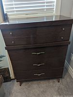 Front view of tall Mid-Century Modern style wooden dresser with four drawers, showing drawer handles and tapered legs.