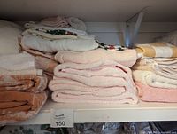 Photo of assorted folded bath towels in pink, peach, white, and patterned orange on a closet shelf.