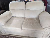 Front view of cream colored two-seater suede sofa showing cushions, armrests and seat area with visible minor wear
