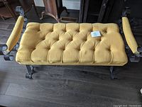 Top view showing yellow tufted fabric seat with armrests on wrought iron bench.