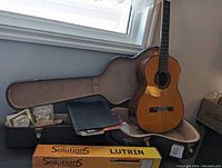 Guitar seated in open plush-lined hardshell case with accessories displayed around it.
