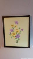 Framed embroidered picture showing the full bouquet of purple and yellow flowers and green stems on a cream fabric background.