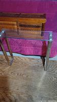 Side view of the tall side table showing glass top and silver legs positioned on wooden floor in front of pink sofa.