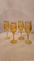 Set of four mid century modern gold-rimmed glass goblets with multicolor abstract designs on gold-tinted glass.
