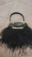 Front view of a small black purse with feather accents and gold-tone MK chain logo detail on flap.