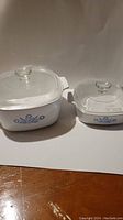 Two vintage Corning Ware casseroles side by side, large and small, both with blue cornflower design and glass lids