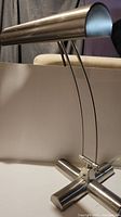 Side view of silver adjustable desk lamp showing its cylindrical head and curved metal arms attached to heavy cross-shaped base.