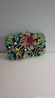 Front view of the small evening bag showing all-over multicoloured crystal floral and leaf patterns on black background.