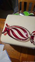 The full view of the red and clear twisted striped glass candy dish on a beige surface, showing the candy wrapper shaped ends and oval body.