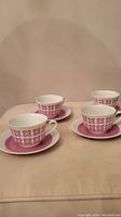 Four vintage Kahla coffee or tea cups each placed on a matching saucer with pink and white geometric floral design.