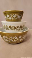 Stacked set of three Pyrex mixing bowls with floral daisy pattern in green and white.