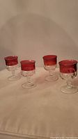 Full view of all four vintage Indiana Glass ruby flash wine glasses showing the ruby red band and textured thumbprint pattern on clear glass base and stem.