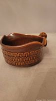 Brown ceramic gravy/sauce boat with textured pattern and handle, angled pouring spout visible