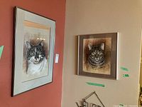 Two framed cat sketches hanging on walls, one larger rectangular with cream and orange matting, one square with brown matting.