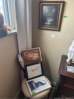 Four framed cat prints displayed in a corner on a chair and wall. Frames vary in style and size.