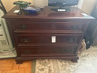 Front view of the mahogany dresser showing three drawers with metal pulls and surface wear.