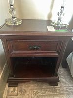 Front view of one mahogany nightstand with drawer and metal pull, showing surface wear and scratches