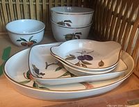 Stack of porcelain bowls and nested trays showing fruit designs and gold trim
