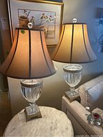 Two crystal urn table lamps on marble top table with beige fabric shades