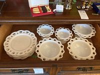 Photo showing six milk glass plates stacked together on the left and five pedestal dishes laid out on the right inside a drawer.