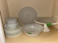 Shelf display of milk glass items including bowls, plates, and a cake stand, showing the overall composition and sizes.