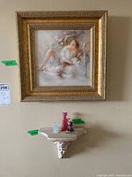 Photo of framed signed print above cherub wall shelf holding three glass cat figurines in pink, light blue, and multicolor