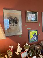 Wall display showing three framed cat prints of various sizes including a realistic cat portrait, a cat with garden pots limited edition, and a colorful stylized cat artwork.