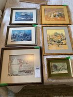 Top-down view of six framed prints with various artistic depictions including a sailboat, village scenes, and a barn. One picture frame backing popped out at the back.