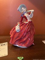Front view of Royal Doulton porcelain figurine showing woman in flowing red dress holding white mask.