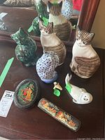 Photo showing various ceramic and resin animal figurines including two brown and white striped cats, two bird figurines, a white seal, and two Russian lacquer trinket boxes.