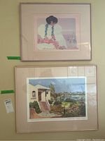 Two framed prints displayed on a wall, one portrait of a woman, one landscape scene.