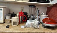 Wide shot of countertop showing various small appliances and kitchen items: blender, crock pot, coffee press, mini grill, and hand mixer.