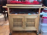 Front view of the rattan tea cart showing the woven double cabinet doors and castor wheels.